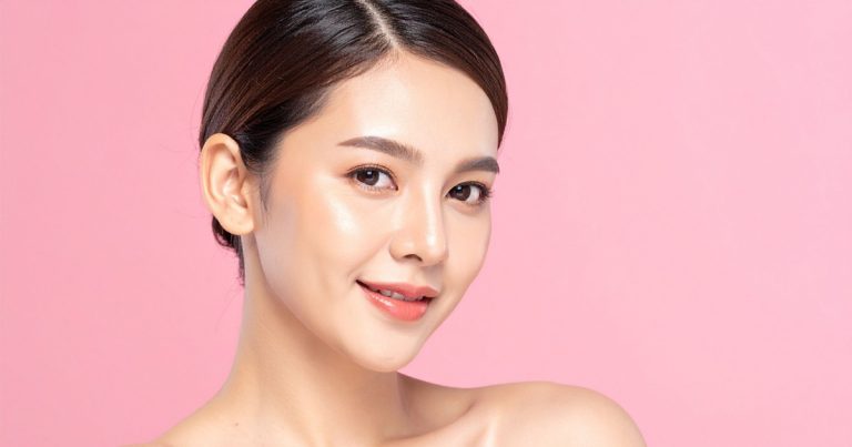 A young woman with clear, glowing skin and natural makeup, smiling softly against a pink background.