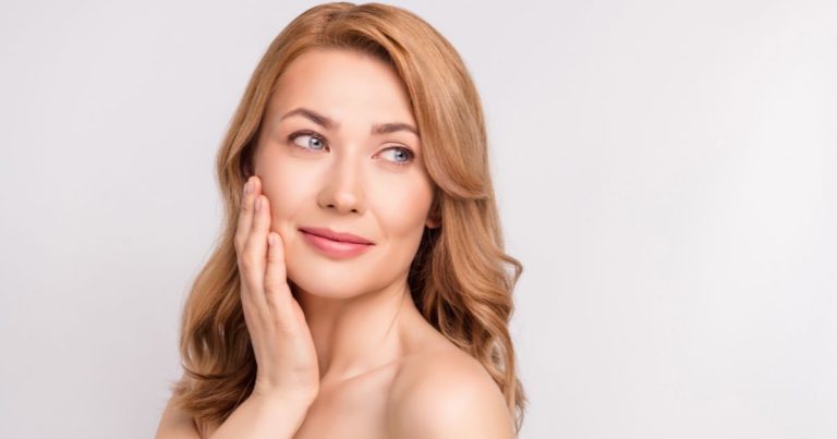 A woman smiling touching her face.